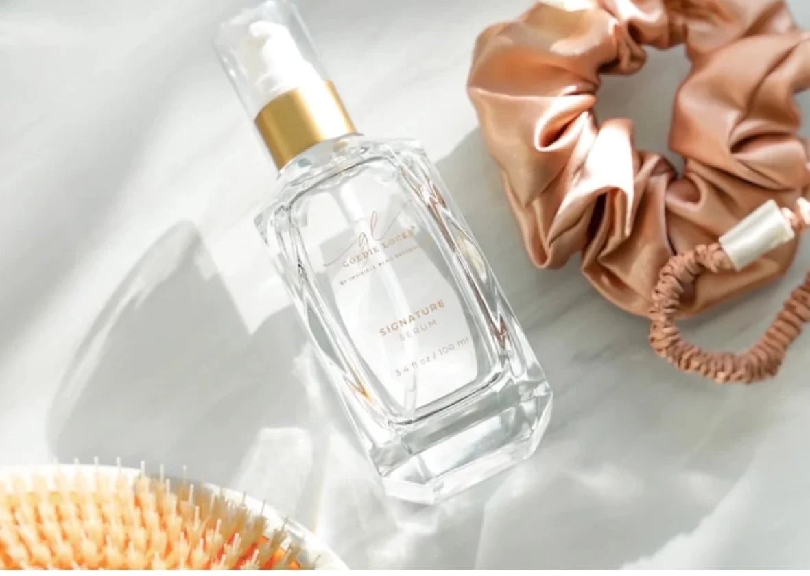 Signature serum bottle, silk scrunchie and boar bristle brush arranged on white marble